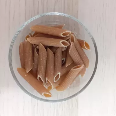 Tigela com massa penne integral castanha clara sobre fundo branco