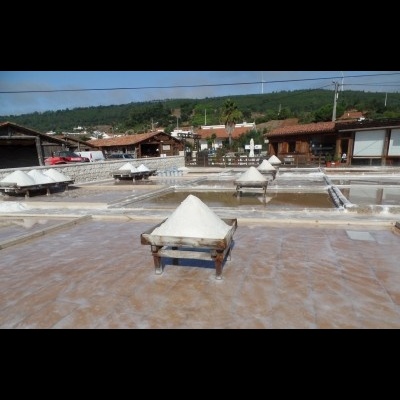 Pilhas de sal branco em tanques de evaporação ao ar livre com casas ao fundo