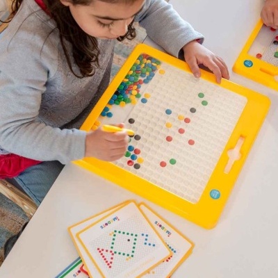 Criança a jogar com tabuleiro amarelo e pinos coloridos em padrão