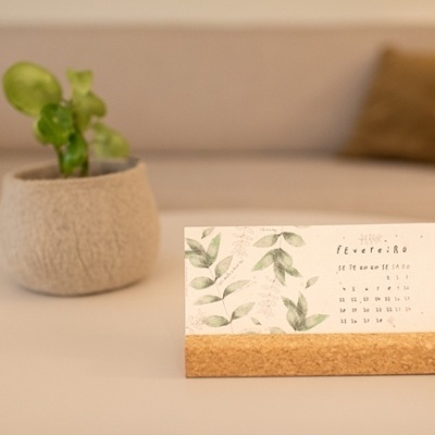 Calendário de mesa com base de cortiça e folha estampada com folhas verdes numa mesa clara