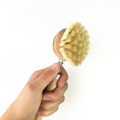 Escova de limpeza com cabo de madeira e cerdas bege segurada por uma mão