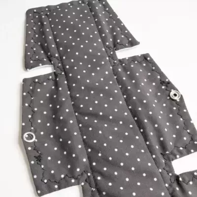 Peça de tecido cinza com bolinhas brancas e ilhóses metálicos sobre fundo branco
