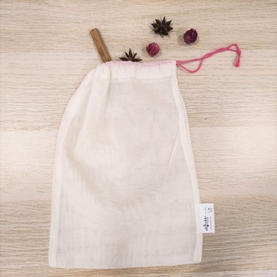 Saco de rede branco com cordão rosa sobre superfície de madeira clara com especiarias e flores