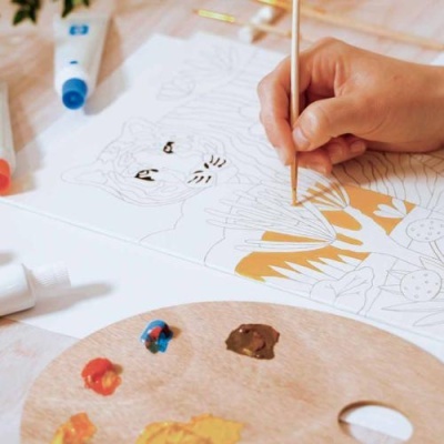 Pessoa pintando desenho de tigre com pincel e paleta de tintas coloridas