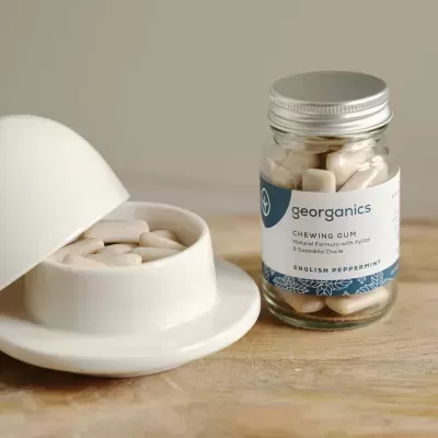 Frasco de vidro com pastilhas de goma Georganics e recipiente branco com tampa aberta