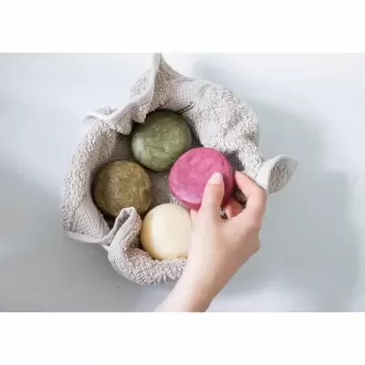 Cesta de tecido com quatro sabonetes sólidos coloridos, mão a segurar sabonete vermelho