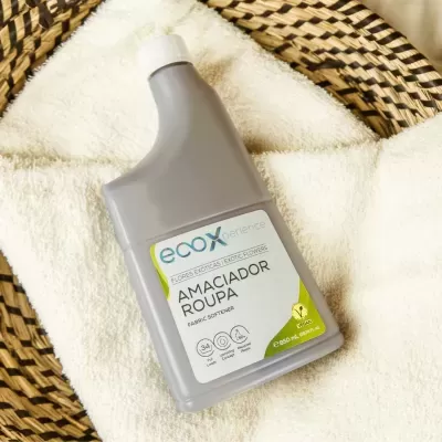 Frasco cinzento de amaciador de roupa ecoXperience sobre toalha creme em cesto trançado