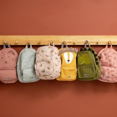 Mochilas infantis coloridas penduradas numa parede castanha