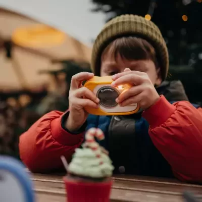 Criança a tirar fotografia com uma câmara amarela em ambiente exterior com um cupcake à frente.