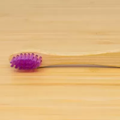 Escova de dentes de madeira com cerdas roxas sobre superfície de madeira
