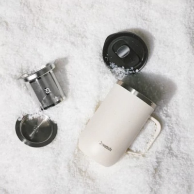 Copo térmico branco com tampa preta e filtro de metal sobre neve