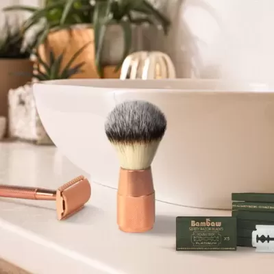 Kit de barbear com pincel, lâmina e sabonete numa bancada branca junto a uma pia oval