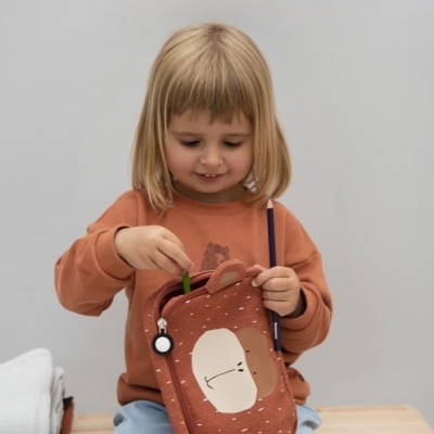 Criança sentada com bolsa de tecido castanho com estampa de rosto e pintinhas brancas