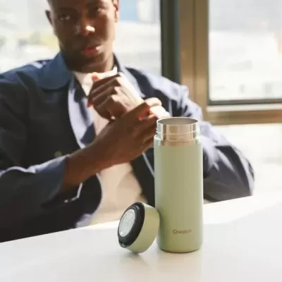 Garrafa térmica verde com tampa preta e mostrador numa mesa branca