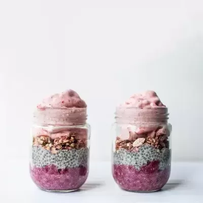 Dois frascos com camadas de purê roxo, chia, granola e creme rosa