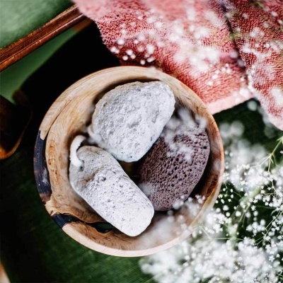 Tigela de madeira com três pedras e pano vermelho ao lado, fundo verde com flores brancas pequenas