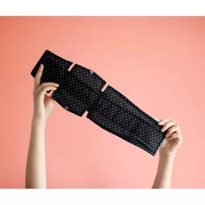 Máscara de tecido preto com pontos brancos segurada por duas mãos