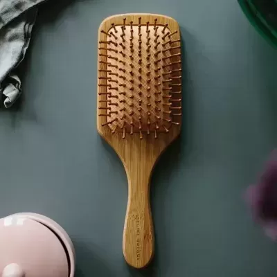 Escova de cabelo de madeira clara com cerdas escuras sobre superfície cinzenta