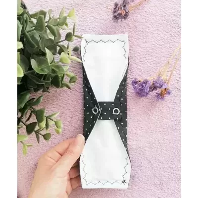 Paleta de papel branca com laço preto de pontos brancos, mão segurando, plantas e flores secas ao fundo