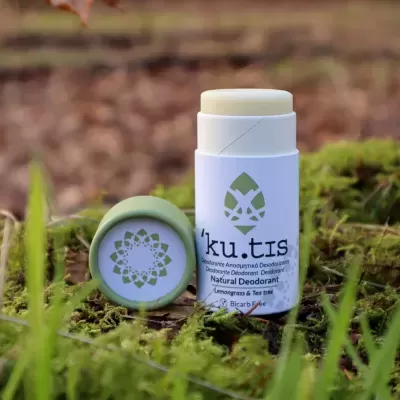 Desodorizante natural em stick com tampa verde e embalagem branca sobre musgo