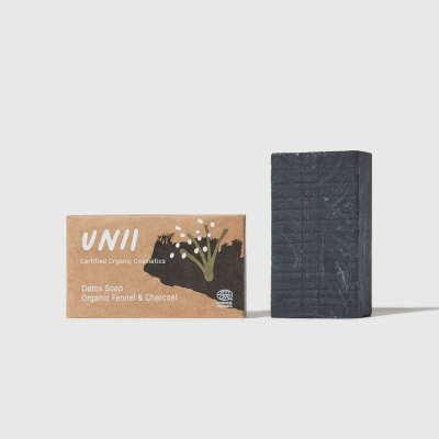 Barra de sabão preta ao lado da embalagem de papel castanho com texto e ilustração de plantas.