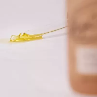 Gota de líquido amarelo translúcido ao lado de frasco bege desfocado