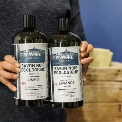 Frascos de sabonete preto ecológico nas mãos de uma pessoa, fundo azul e caixa de madeira.