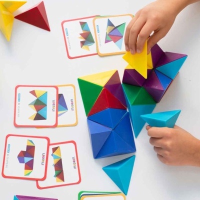Mãos infantis a montar blocos triangulares coloridos com cartas de desafios ao fundo