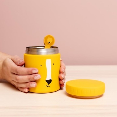 Garrafa térmica amarela com rosto de urso e colher decorativa numa mesa de madeira clara