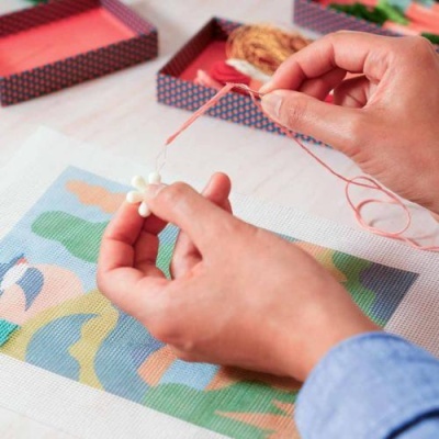 Mãos bordando flor branca com linha cor-de-rosa em tecido colorido
