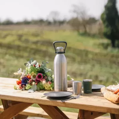 Garrafas térmicas, flores, pratos e copos numa mesa de madeira ao ar livre