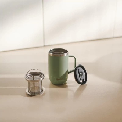 Caneca térmica verde com filtro metálico e tampa preta em superfície clara