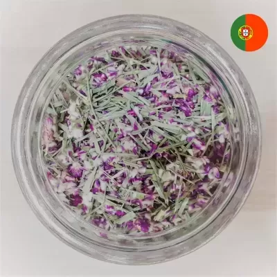Frasco de vidro visto de cima com ervas secas verdes e flores roxas