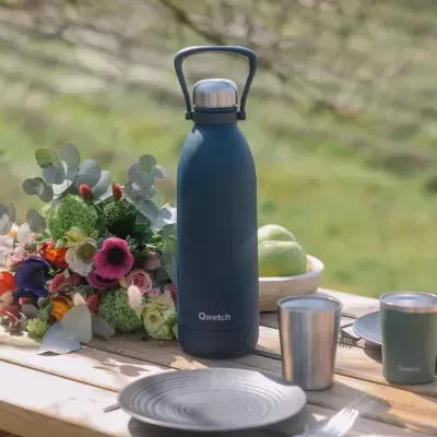 Garrafa térmica azul escura de aço inoxidável com tampa prateada na mesa ao ar livre