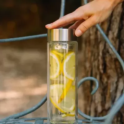 Garrafa de vidro com limão e água sobre mesa metálica ao ar livre