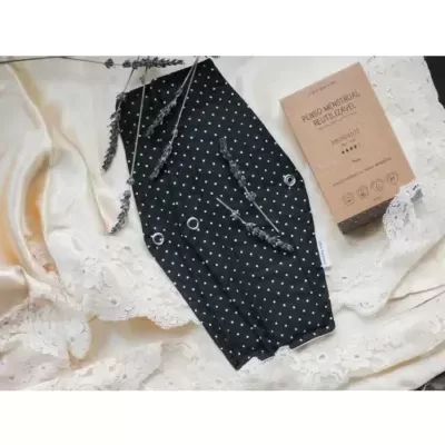 Máscara preta com pontos brancos ao lado de caixa castanha sobre tecido creme com renda