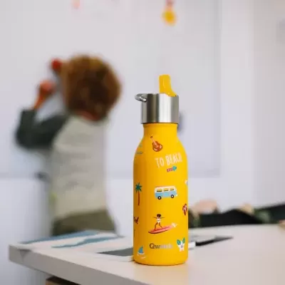 Garrafa amarela decorada com tema de praia sobre mesa branca com criança desfocada ao fundo