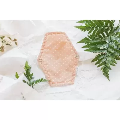 Absorvente de tecido cor de pêssego com pontos brancos e botões de pressão