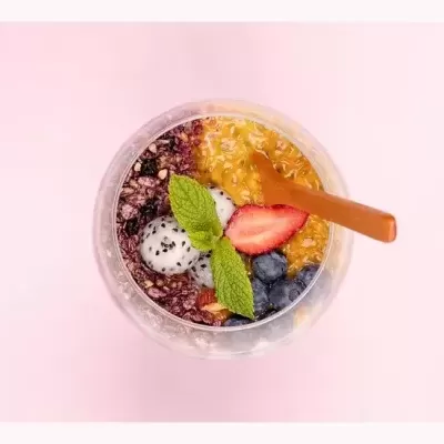 Taça de vidro com mistura colorida e colher de madeira sobre fundo rosa claro