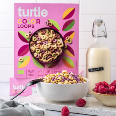 Pacote de cereais coloridos Turtle Color Loops com tigela de cereais, framboesas e garrafa de cashew em fundo branco
