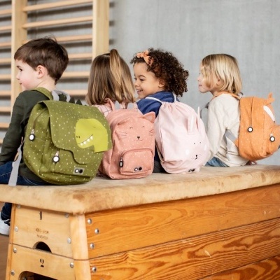 Crianças sentadas de costas com mochilas coloridas numa sala de ginástica