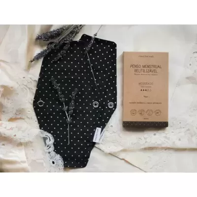 Penso menstrual reutilizável preto com padrão de pontos brancos e caixa castanha com texto em português sobre tecido de renda creme