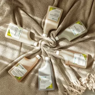 Seis garrafas de produtos ECOX para roupa dispostas em círculo sobre tecido bege com padrão geométrico