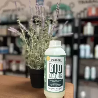 Frasco de detergente BIO MACH em superfície de madeira com planta e prateleiras desfocadas ao fundo