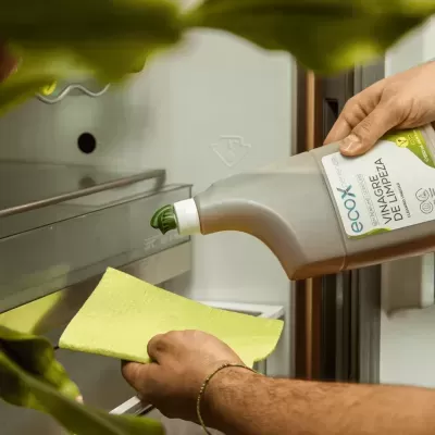 Pessoa a despejar vinagre de limpeza num pano amarelo dentro de uma geladeira branca