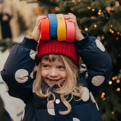 Menina com casaco e gorro segurando bandas de silicone coloridas na cabeça