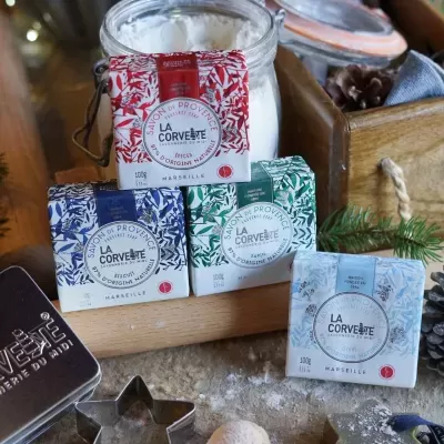 Sabonetes La Corvette de Provence em embalagens vermelha, verde, azul e azul claro junto a jarro de vidro e elementos naturais