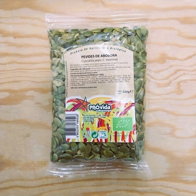 Saco transparente com sementes de abóbora verdes e etiqueta colorida sobre superfície de madeira clara