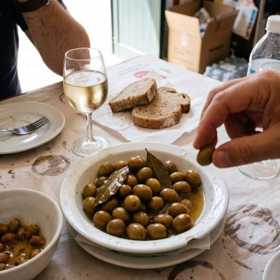 White bowl with green olives, glass of wine, slices of bread on table