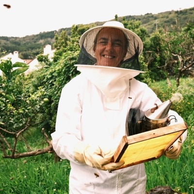 Beekeeper in white suit holding honeycomb frame and bee smoker in a garden